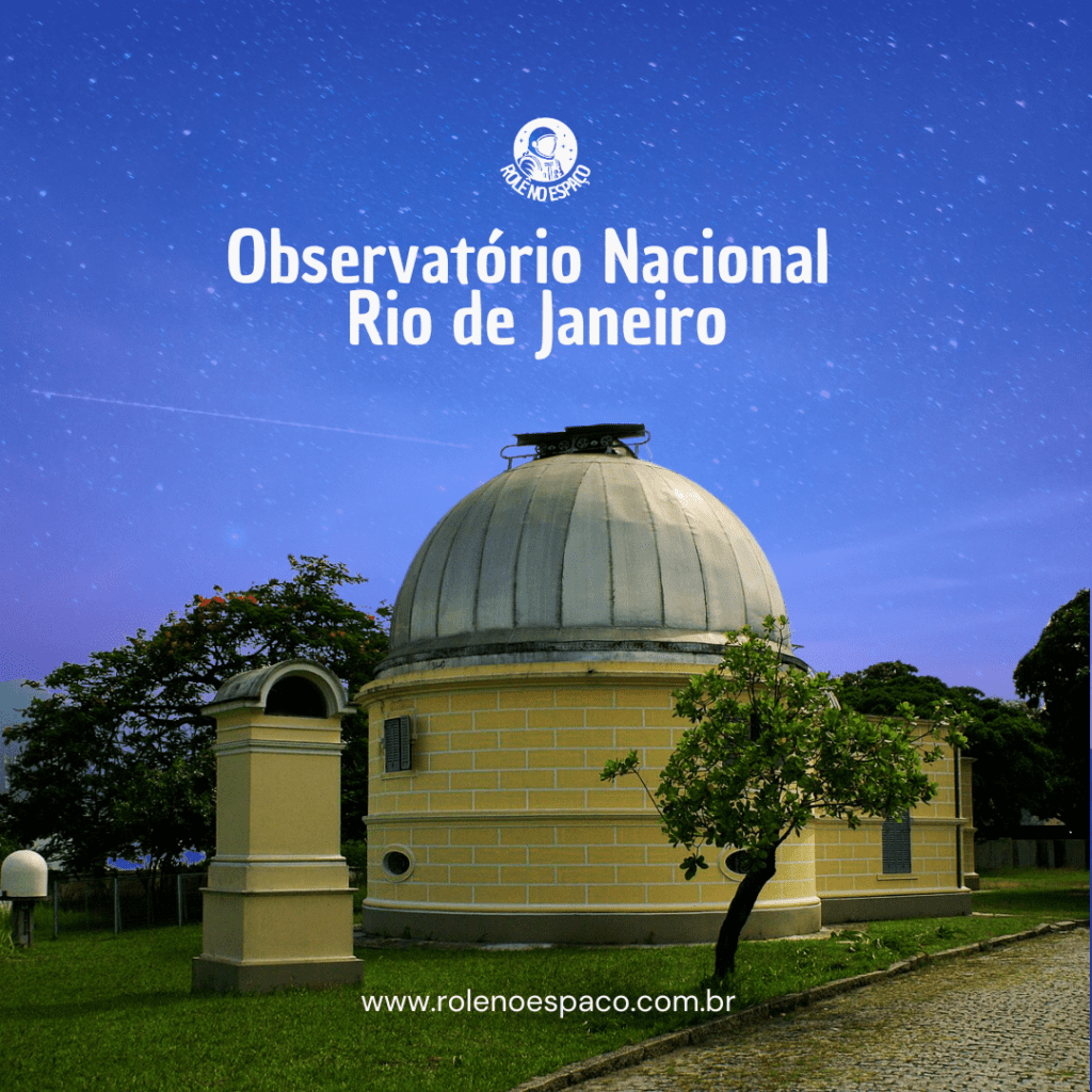 "Imagem do Observatório Nacional no Rio de Janeiro, com a cúpula de avistamento visível e a estrutura de tijolos amarelos. A cúpula branca destaca-se contra o céu estrelado. O edifício está cercado por árvores e uma grama verde, criando um cenário tranquilo e perfeito para a observação astronômica