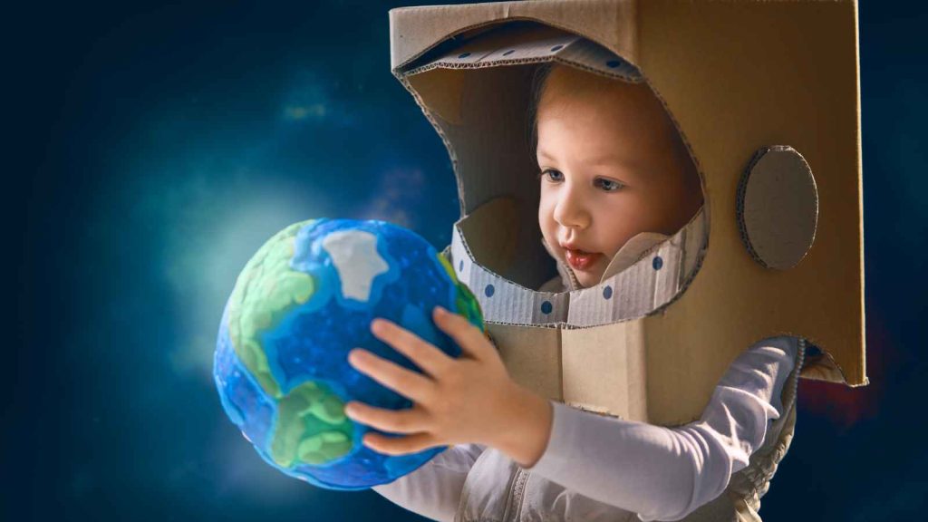 Criança com traje de astronauta, segurando uma réplica do planeta Terra, ilustrando a importância da astronomia no ensino fundamental e despertando o interesse pela ciência espacial.