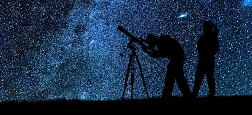 Astrônomo observando estrelas com um telescópio sob um céu estrelado