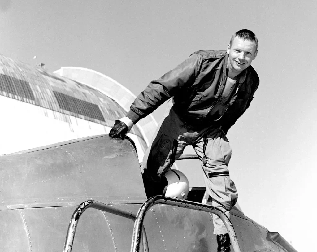 Antes de se tornar astronauta, Neil Armstrong era piloto de testes. Na imagem, ele aparece saindo do avião experimental X-14 com um grande sorriso no rosto. O capacete parece estar apoiado no painel da aeronave, refletindo sua experiência na aviação antes da era espacial.