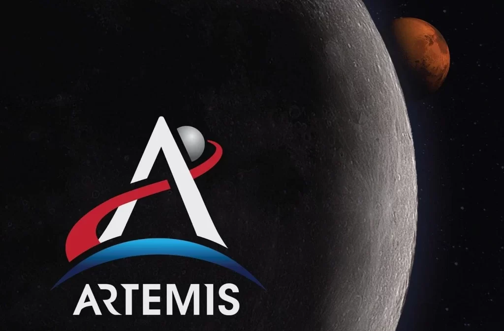 logo do programa Artemis da NASA. O logo apresenta a letra 'A' central, com um caminho vermelho sinuoso que passa entre as letras, conectando as formas de maneira fluída. No topo da letra 'A', há um ícone da Lua, representado por um círculo com detalhes que lembram sua superfície craterada. Ao fundo, a imagem revela a circunferência da Lua, iluminada parcialmente, como se estivesse sendo vista do espaço. Mais distante, no horizonte cósmico, está o planeta Marte, visível como um ponto vermelho, com sua superfície levemente visível, destacando-se contra o fundo negro do espaço. O contraste entre o vermelho do caminho, o brilho da Lua e a presença de Marte cria uma sensação de profundidade no espaço.