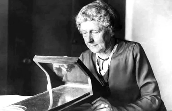 Annie Jump Cannon, uma astrônoma pioneira, observando um equipamento de madeira e vidro que ajudava na classificação das estrelas. Na imagem em preto e branco, ela aparece idosa, vestindo trajes típicos da época, com um olhar atento enquanto ajusta o dispositivo que contribuiu para o sistema de classificação estelar.