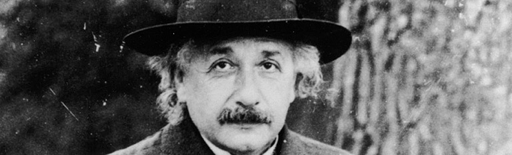 Imagem de Albert Einstein em um retrato de perfil, usando um chapéu preto e roupas de frio. Seu rosto é parcialmente visível, destacando seu icônico bigode espesso e cabelo desgrenhado. Ele exibe uma expressão séria e focada, típica de suas fotos formais. A iluminação suave destaca os contornos de seu rosto e a parte inferior do chapéu, enquanto o fundo permanece neutro. A roupa de frio sugere um clima mais frio, adicionando uma sensação de sofisticação ao seu estilo característico.