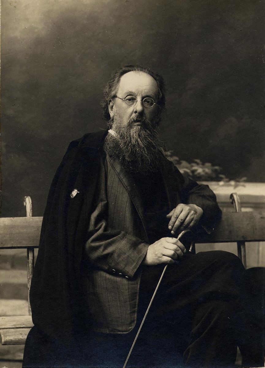 Konstantin Tsiolkovski, um homem idoso com uma longa barba branca e óculos redondos, está sentado em um banco. Ele segura uma bengala com as mãos, transmitindo uma postura serena e contemplativa. Considerado um dos pioneiros da astronáutica, suas ideias ajudaram a moldar o futuro das viagens espaciais.