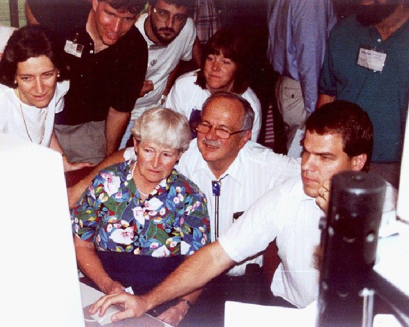 Carolyn e Gene Shoemaker se reúnem em volta de um computador com outras pessoas em 16 de julho de 1994 para ver as primeiras imagens dos fragmentos do cometa Shoemaker-Levy 9 colidindo com Júpiter. As imagens foram exibidas em um monitor no Instituto de Ciência do Telescópio Espacial em Baltimore, Maryland. Credito NASA