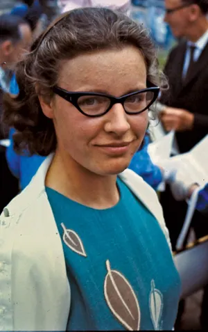 magem de Jocelyn Bell Burnell, astrônoma e descobridora de pulsares, usando camiseta azul, terno cinza e óculos de grau pretos, sorrindo em ambiente acadêmico.