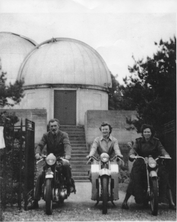 Figura 1. C. C. L. Gregory (à esquerda) em sua "moto enorme e potente", com Margaret e Anne Carew Robinson (à direita), funcionária do Observatório de Mill Hill, por volta de 1950. Margaret escreveu (25): “Eu tinha investido em uma moto fácil de pilotar (velocidade máxima: 45 mph…). Ela também tinha um assento de garupa. Gerard [de Vaucouleurs] costumava sentar na garupa enquanto eu o levava até o apartamento que ele e Antoinette alugavam, após uma noite de observação.” Fotografia cortesia do Observatório de Mill Hill, Universidade de Londres.