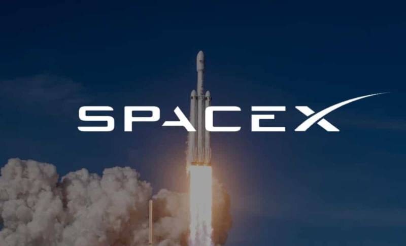 Logo da SpaceX em destaque com o foguete Falcon Heavy decolando rumo ao espaço, deixando um rastro de fumaça contra o céu ao fundo