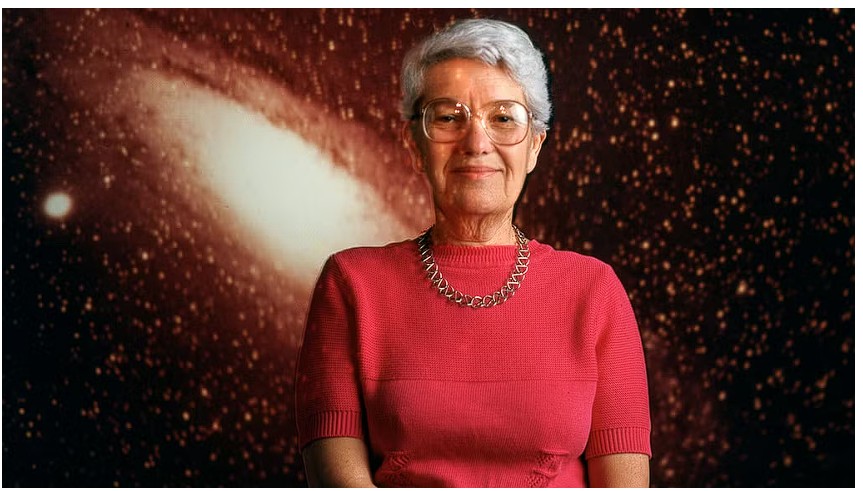 vera Rubin usando uma roupa vermelha, com cabelos grisalhos e curtos, e óculos. Ela usa um colar no pescoço, transmitindo um ar de sofisticação. Ao fundo, uma galáxia em tons alaranjados, ressaltando sua conexão com o campo da astronomia e a vastidão do universo que ela ajudou a explorar.