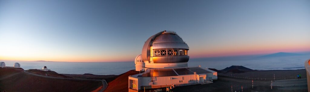 Vista panorâmica do telescópio Gemini North ao pôr do sol, com nuvens ao fundo. O telescópio, parte do Observatório Internacional Gemini, está localizado a 4.200 metros de altitude (13.825 pés) no Havaí.