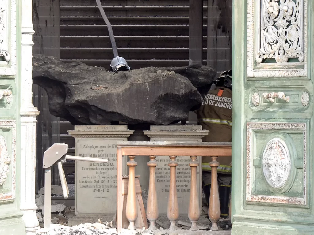 O Meteorito Bendegó no centro da imagem, resistindo às altas temperaturas do incêndio no Museu Nacional em São Cristóvão, Rio de Janeiro, em 03/09/2018. Ao redor, bombeiros combatem as chamas na entrada do museu que está em chamas.