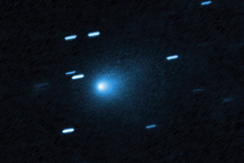 No centro da imagem está um cometa que se apresenta como um casulo azulado em formato de gota, formado por poeira que se desprende do núcleo sólido e gelado do cometa, visto contra um fundo preto. O cometa parece estar se movendo em direção ao canto inferior esquerdo da imagem. Cerca de uma dúzia de rastros diagonais curtos e azul-claro estão espalhados pela imagem — são estrelas de fundo que pareceram se mover durante a exposição, já que o telescópio estava acompanhando o movimento do cometa.