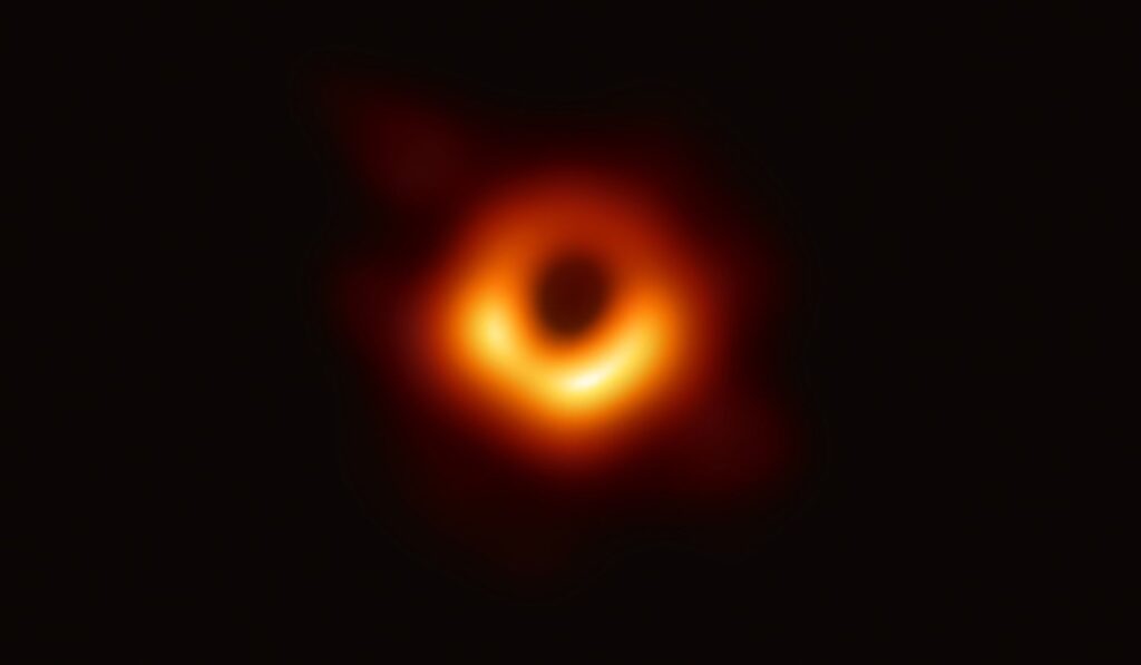 Primeira imagem real de um buraco negro, capturada em 2019 pelo projeto Event Horizon Telescope, mostrando a silhueta do buraco negro da galáxia M87 com um anel de luz brilhante ao redor da sua sombra.