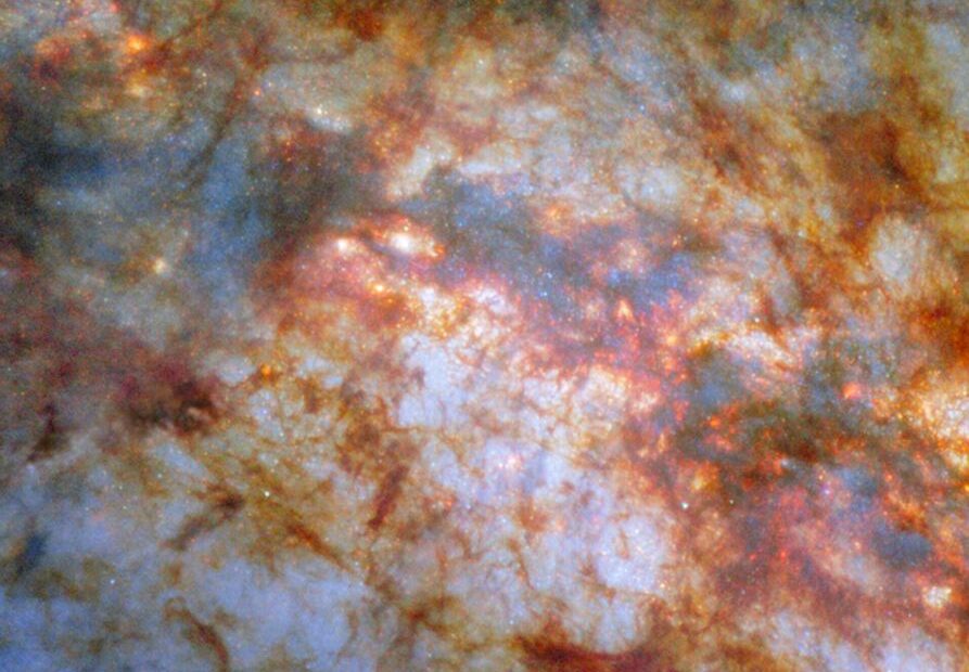 Uma visão aproximada do centro da galáxia M82. A luz azulada e brilhante que emana do centro é resultado da formação ativa de estrelas naquela região. Uma espessa faixa de gás — preta no centro e avermelhada nas bordas — cruza o núcleo e bloqueia grande parte da luz. Filamentos mais finos e aglomerados de poeira avermelhada cobrem grande parte do restante da visão.