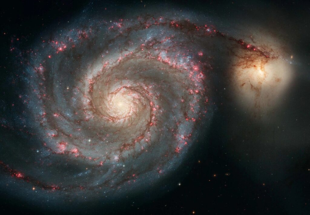 A Galáxia do Redemoinho, M51, é uma galáxia espiral localizada a 31 milhões de anos-luz de distância. Ela destaca os atributos de uma galáxia espiral típica, incluindo braços graciosos e curvos, regiões cor-de-rosa de formação estelar e brilhantes filamentos azuis de aglomerados estelares.