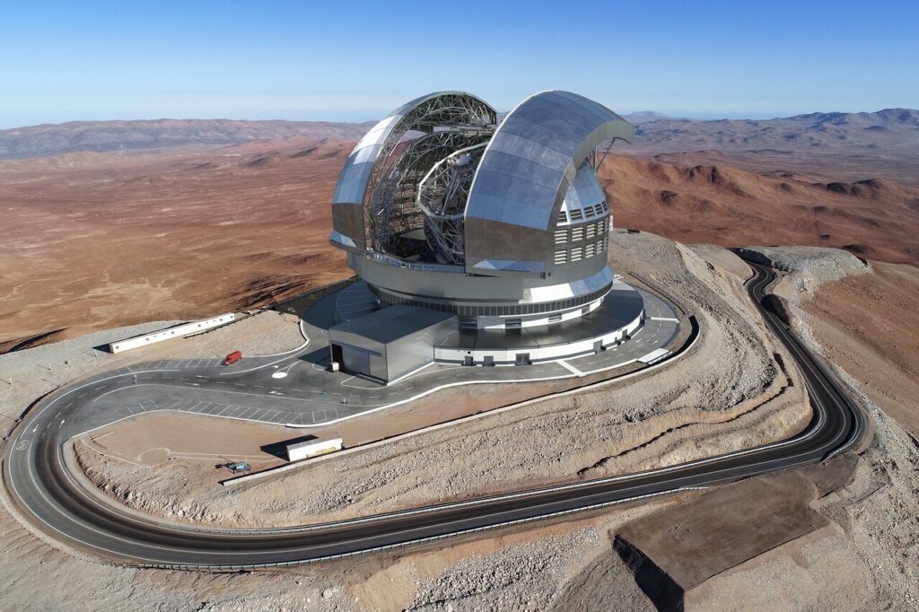 O Extremely Large Telescope (ELT) será instalado no topo do Cerro Armazones, a aproximadamente 3.046 metros de altura no Deserto do Atacama, no Chile, cercado por vistas deslumbrantes das planícies abaixo.
Esta imagem (uma ilustração artística) mostra como o telescópio ficará no topo da montanha. O nivelamento do cume do Cerro Armazones, em preparação para a construção do ELT, foi concluído em 2015.