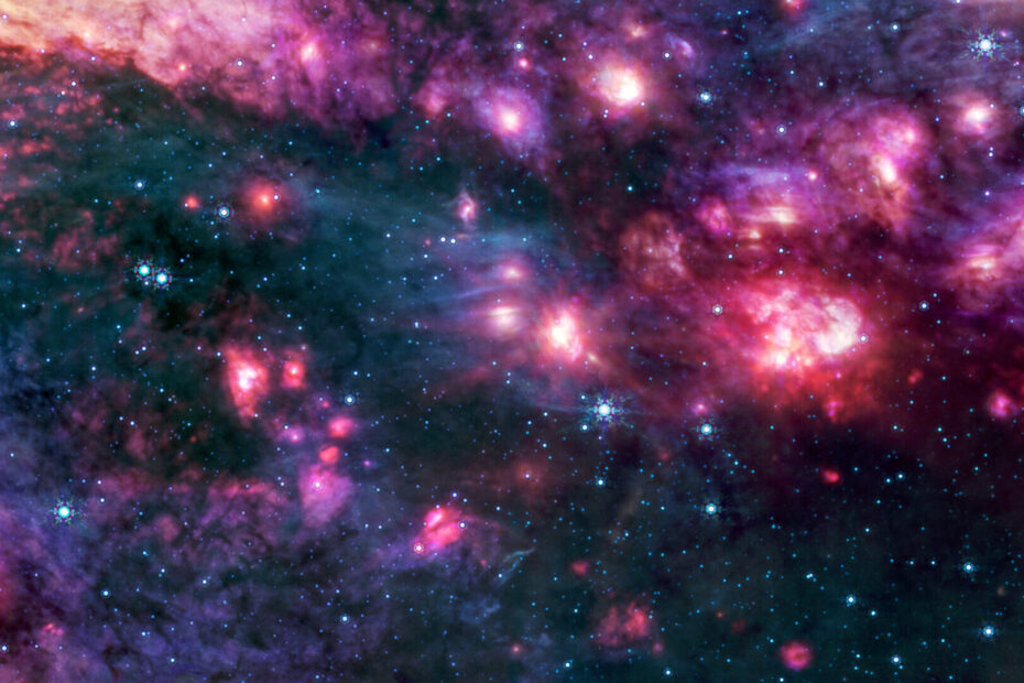 Nuvens cósmicas em tons de rosa e roxo, algumas com centros brilhantes, estão cercadas por áreas escuras que se assemelham ao espaço negro pontilhado por estrelas azul-azuladas. Um grupo de pequenas nuvens à direita é mais avermelhado do que qualquer outra região da imagem.