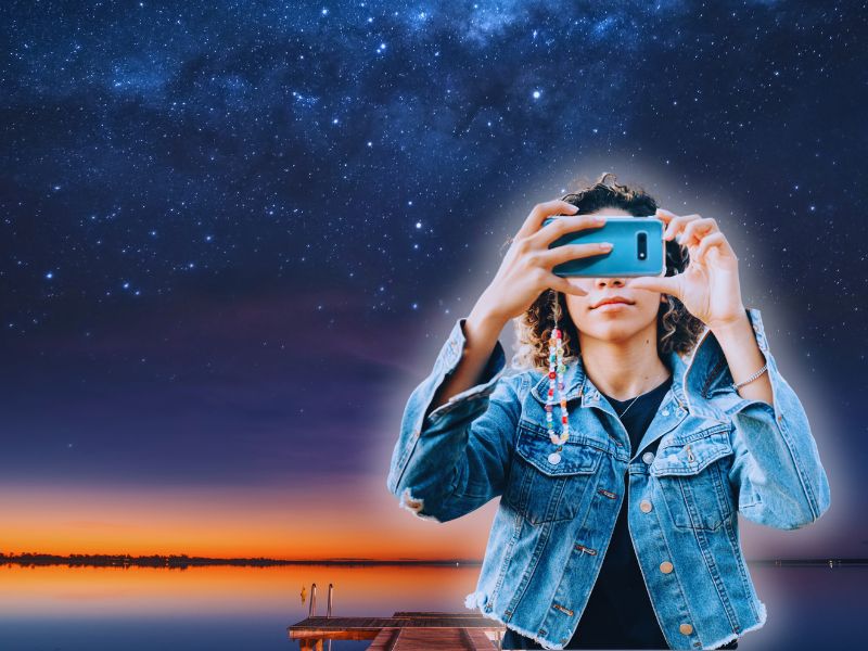 Mulher tirando uma astrofoto com o celular sob um céu estrelado, capturando a beleza das estrelas e o encanto da astronomia amadora.