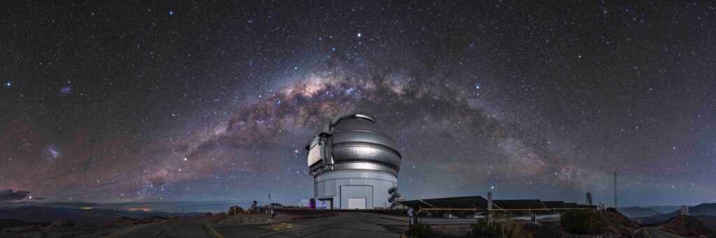 O telescópio Gemini Sul no topo do Cerro Pachón, no Chile, com sua cúpula iluminada sob um arco brilhante da Via Láctea no céu. A imagem destaca a localização remota do observatório e o céu profundamente estrelado. Crédito: Gemini/NOIRLab/NSF/AURA/Kwon O Chul. Créditos: Gemini/NOIRLab/NSF/AURA/Kwon O Chul
