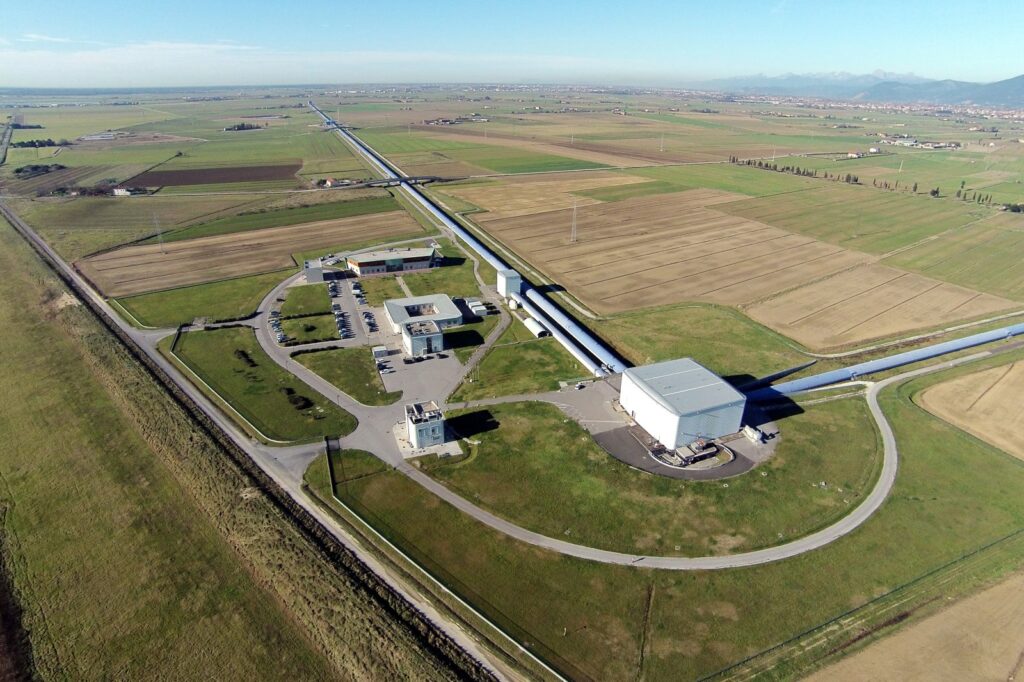 Vista aérea do interferômetro Virgo, na Itália, mostrando seus longos túneis brancos em formato de “L” em meio a uma área verde aberta. A imagem representa a capacidade do observatório de detectar ondas gravitacionais, incluindo as que poderiam ser produzidas por tecnologia extraterrestre avançada, segundo um novo estudo. Créditos: Virgo Collaboration.