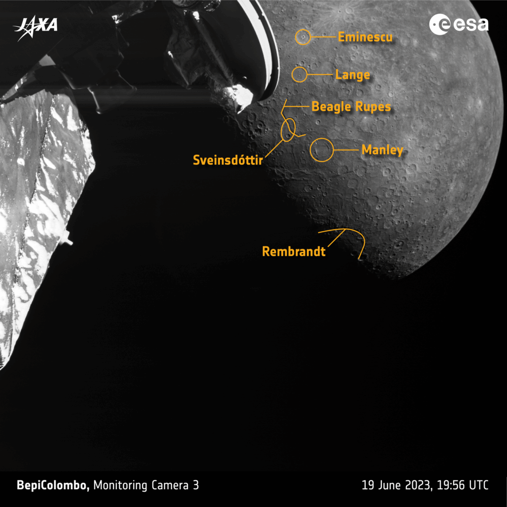 Imagem em preto e branco de Mercúrio mostrando crateras antigas, escarpas e a bacia Raditladi. No primeiro plano aparecem a antena de alto ganho e parte do corpo da BepiColombo. Destaques incluem Manley Crater, Beagle Rupes e Challenger Rupes, além de raios brilhantes de crateras mais jovens.