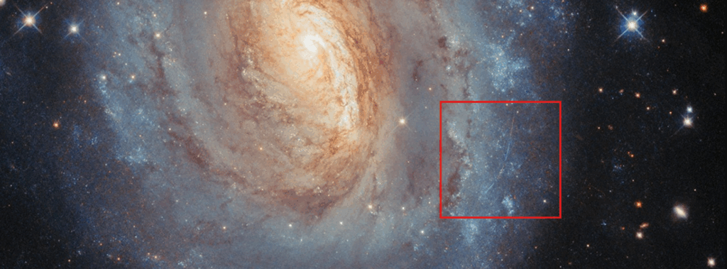 Close-up do lado direito da galáxia espiral NGC 6000, mostrando quatro trilhas finas em amarelo e azul atravessando o campo de visão. As trilhas, que aparecem segmentadas e em cores alternadas, correspondem ao rastro de um asteroide do Sistema Solar capturado em quatro exposições separadas do Telescópio Espacial Hubble, cada uma registrada com filtros diferentes