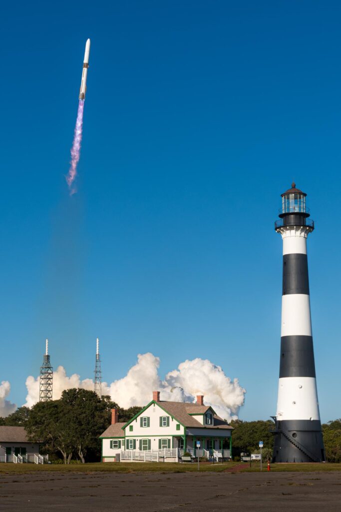 Lançamento do foguete New Glenn visto próximo ao Farol de Cape Canaveral, com a coluna de fumaça ascendendo enquanto a missão ESCAPADE da NASA decola rumo a Marte.