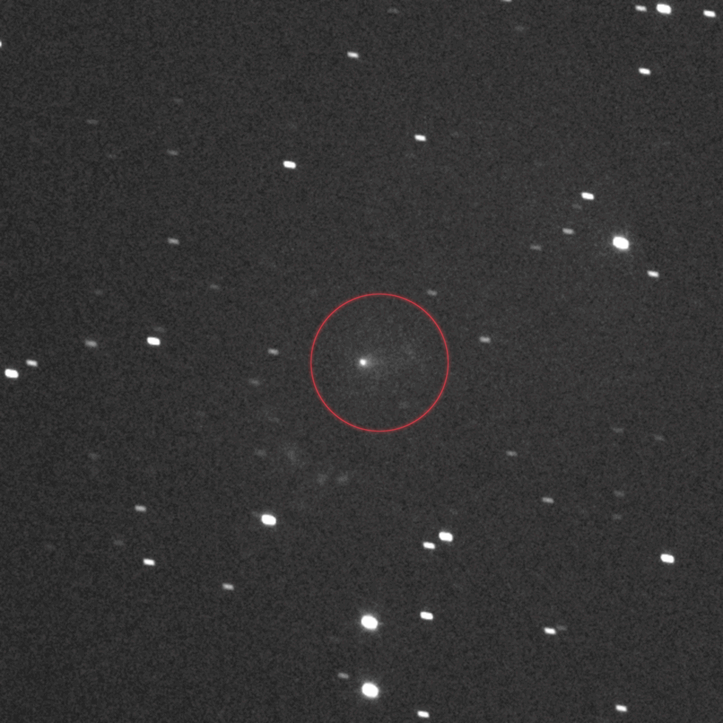 Imagem em preto e branco mostrando o cometa interestelar 3I/ATLAS no centro, destacado por um círculo. A câmera L’LORRI da espaçonave Lucy capturou sua coma brilhante e a cauda tênue estendida para a direita. A cena resulta da combinação de várias fotos tiradas em 16 de setembro de 2025, enquanto o cometa avançava em direção a Marte. A imagem cobre uma área equivalente a um terço da largura da Lua cheia.