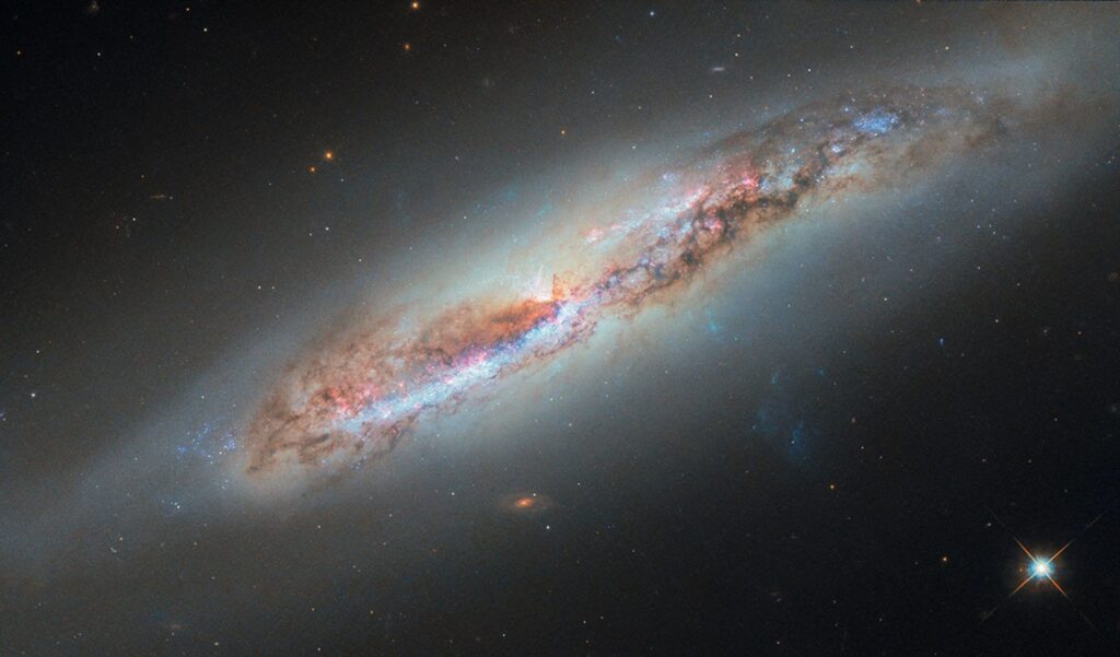 Imagem do Telescópio Espacial Hubble mostrando a galáxia espiral NGC 4388 vista quase de perfil, com uma pluma de gás ionizado sendo arrancada do disco enquanto a galáxia se move pelo aglomerado de Virgem.