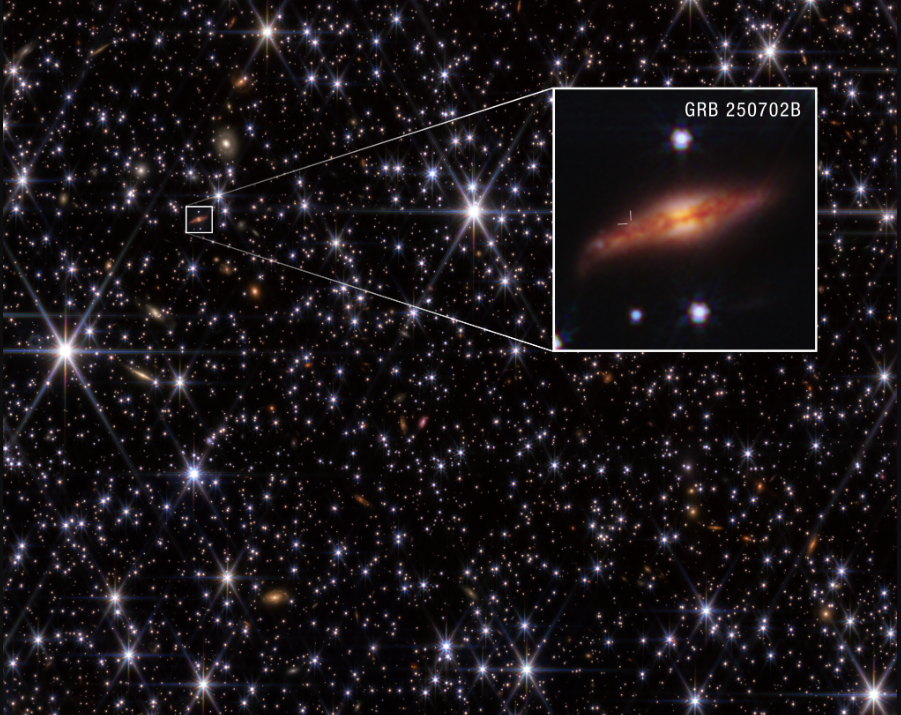 Imagem do telescópio James Webb mostrando a galáxia hospedeira do GRB 250702B, localizada a cerca de 8 bilhões de anos-luz. Um zoom indica a posição do surto próximo à borda superior da faixa de poeira escura da galáxia, afastando a possibilidade de ligação com o buraco negro supermassivo central.
