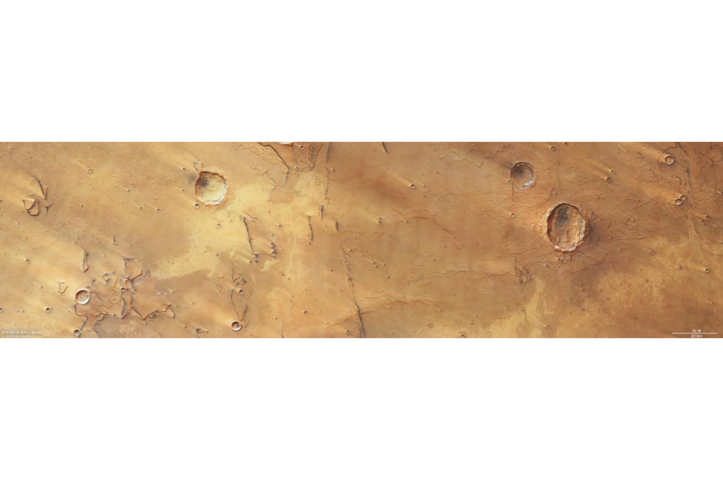 Imagem colorida da região de Hesperia Planum em Marte, mostrando uma grande cratera de impacto em formato de borboleta. A cratera elíptica apresenta bordas irregulares, interior sombreado e extensão alongada, destacando-se sobre a planície marciana amarelada e avermelhada.