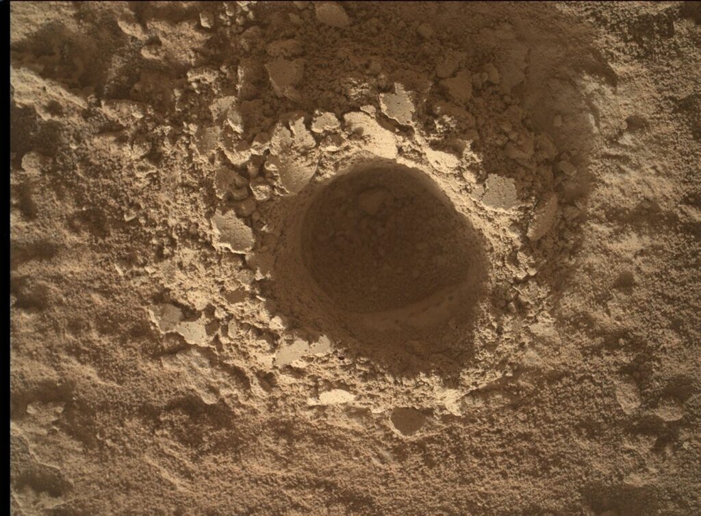 Imagem capturada pelo rover Curiosity em Marte com a c&acirc;mera MAHLI, mostrando uma vis&atilde;o aproximada da superf&iacute;cie marciana. O enquadramento revela detalhes do solo, incluindo gr&atilde;os, rachaduras e texturas rochosas em alta resolu&ccedil;&atilde;o. A ilumina&ccedil;&atilde;o destaca as varia&ccedil;&otilde;es de cor e estrutura do terreno, caracter&iacute;sticas usadas pela equipe cient&iacute;fica para an&aacute;lises geol&oacute;gicas.