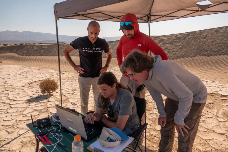 Pesquisadores do JPL reunidos sob uma tenda no Death Valley monitoram o desempenho de um drone de pesquisa equipado com software de navegação para futuras missões em Marte.