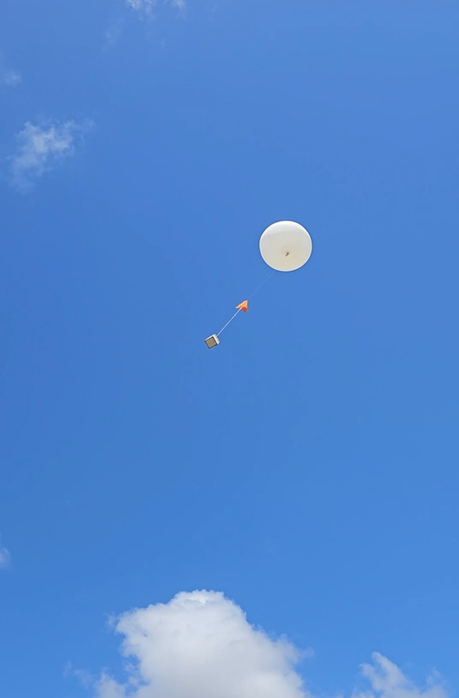 Balão estratosférico branco em voo na estratosfera, destacando-se em contraste com o céu azul durante teste de tecnologia ambiental.