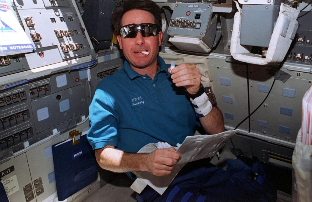 Astronauta da NASA Stephen K. Robinson coleta amostra de saliva com swab a bordo do ônibus espacial Discovery durante experimento biológico.