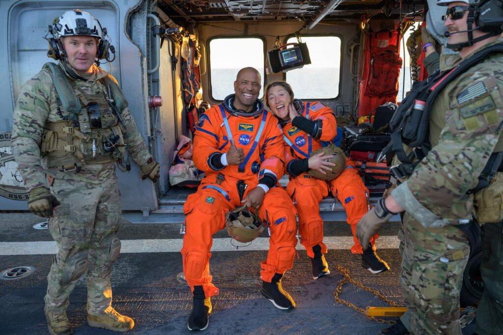 Astronautas Victor Glover e Christina Koch sentados em helicóptero Seahawk após resgate da missão Artemis II no USS John P. Murtha