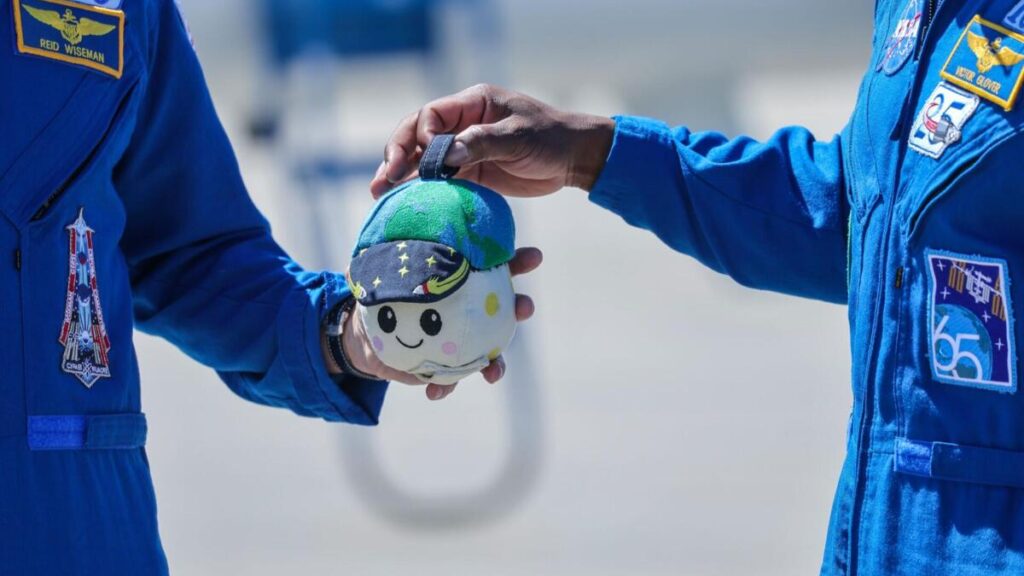 Astronautas da missão Artemis II seguram o indicador de gravidade zero “Rise” durante preparação com trajes da NASA