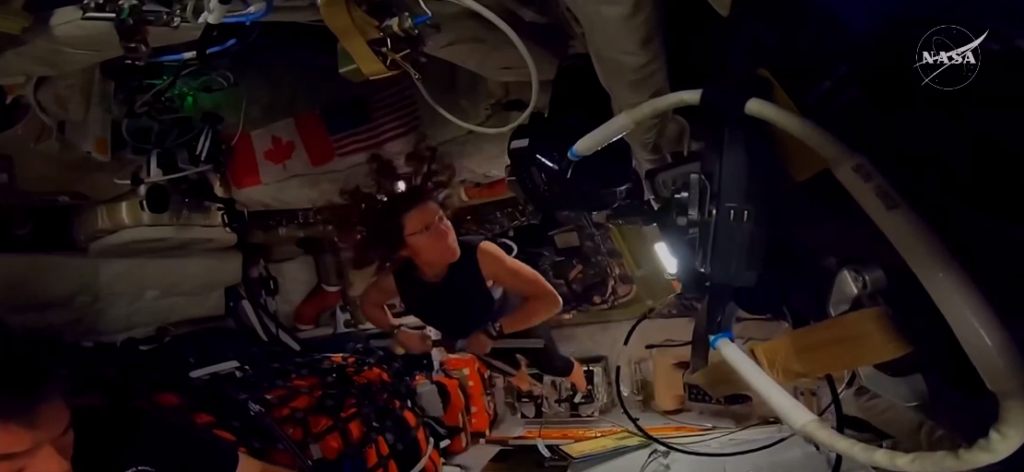 Astronauta Christina Koch realizando exercício para o ombro dentro da nave Orion durante a missão Artemis II em microgravidade