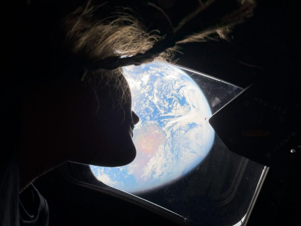 Astronauta Christina Koch observando a Terra pela janela da cápsula Orion spacecraft durante a missão Artemis II a caminho da Lua