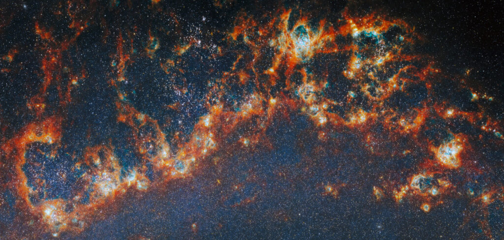 Imagem do telescópio James Webb mostrando regiões de formação estelar no braço espiral da galáxia M51, com nuvens brilhantes de gás e poeira em vermelho e laranja cercando aglomerados de estrelas jovens.