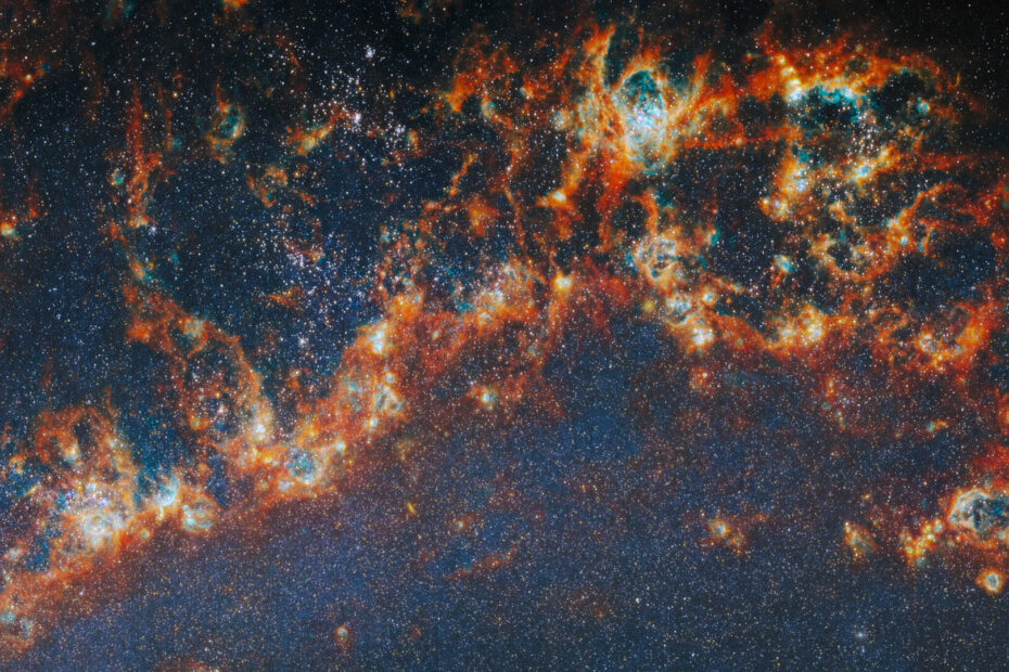 Imagem do telescópio James Webb mostrando regiões de formação estelar no braço espiral da galáxia M51, com nuvens brilhantes de gás e poeira em vermelho e laranja cercando aglomerados de estrelas jovens.