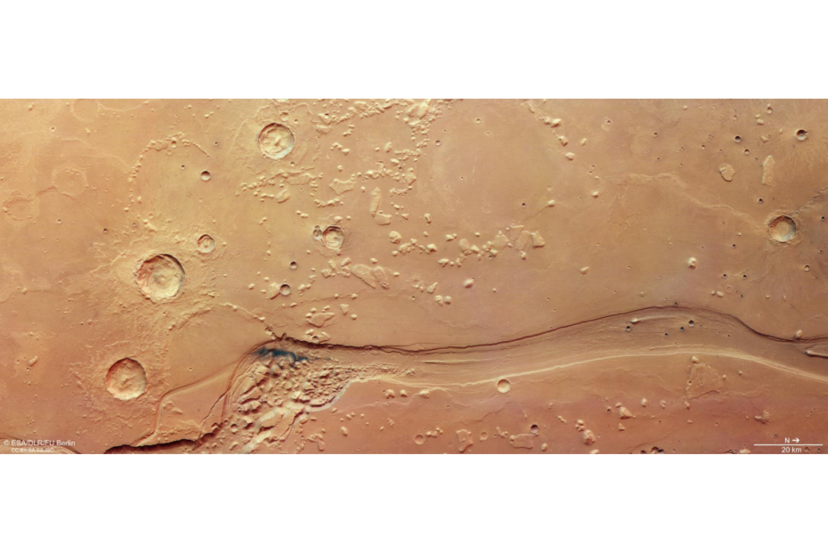 Imagem aérea de Shalbatana Vallis em Marte mostrando um grande canal sinuoso cercado por crateras e terreno caótico, registrado pela sonda Mars Express da ESA.